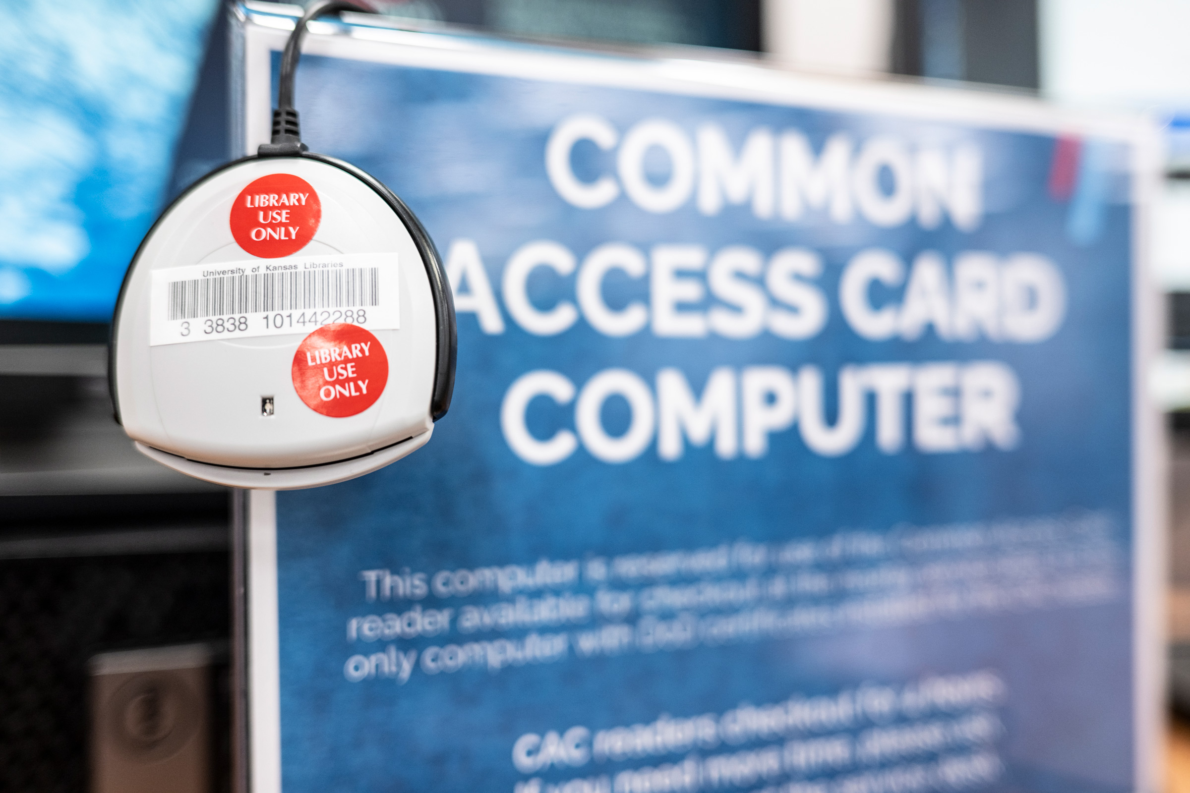 A Common Access Card reader hangs on the edge of the Common Access Card Computer signage in Watson Library.